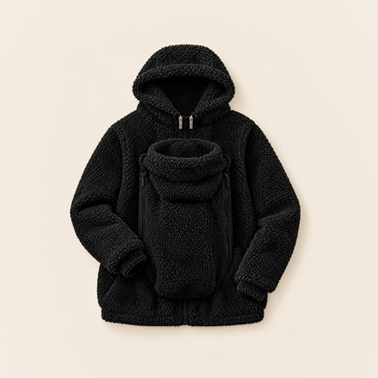 Schwarze 2-in-1 Kuscheljacke aus Teddyfleece mit Kapuze und eingesetztem Babyeinsatz, liegend auf cremefarbenem Hintergrund